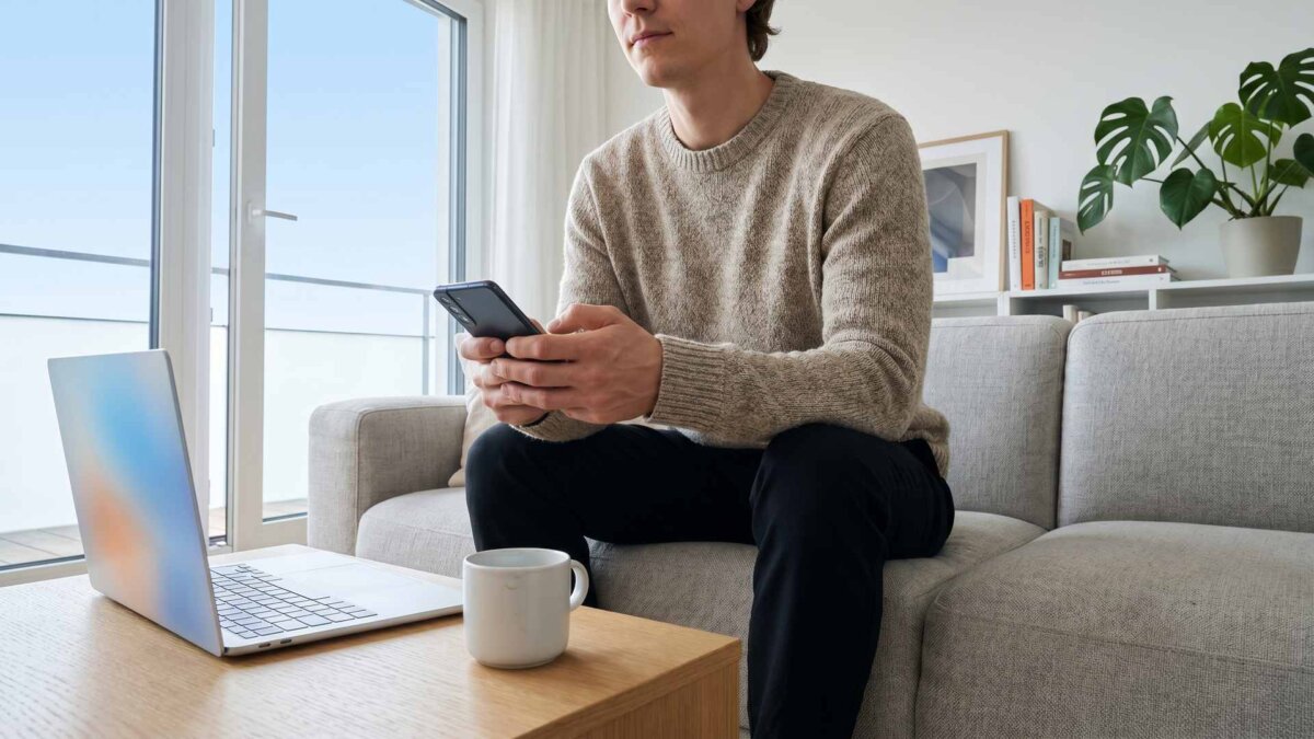 Person auf dem Sofa bucht mit Smartphone, Laptop auf dem Couchtisch