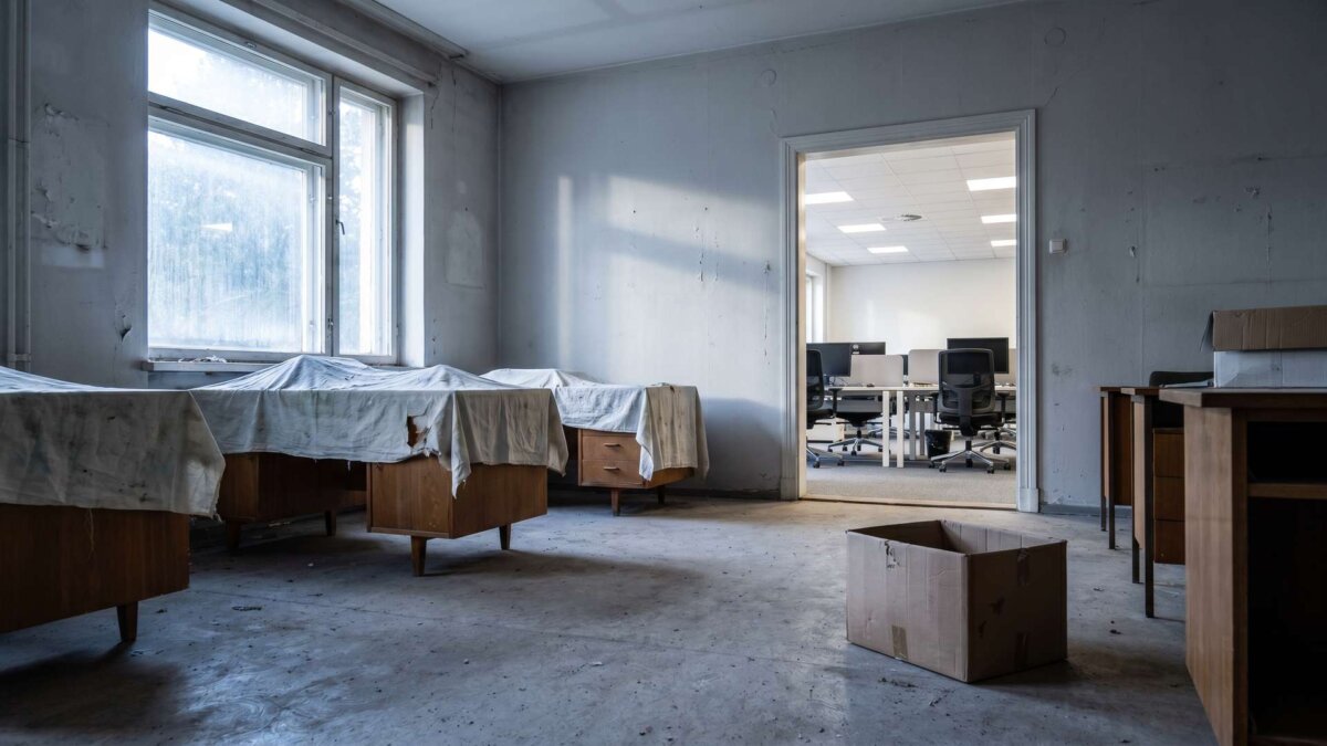 Leeres stillgelegtes Büro mit abgedeckten Schreibtischen, dahinter ein helles Büro