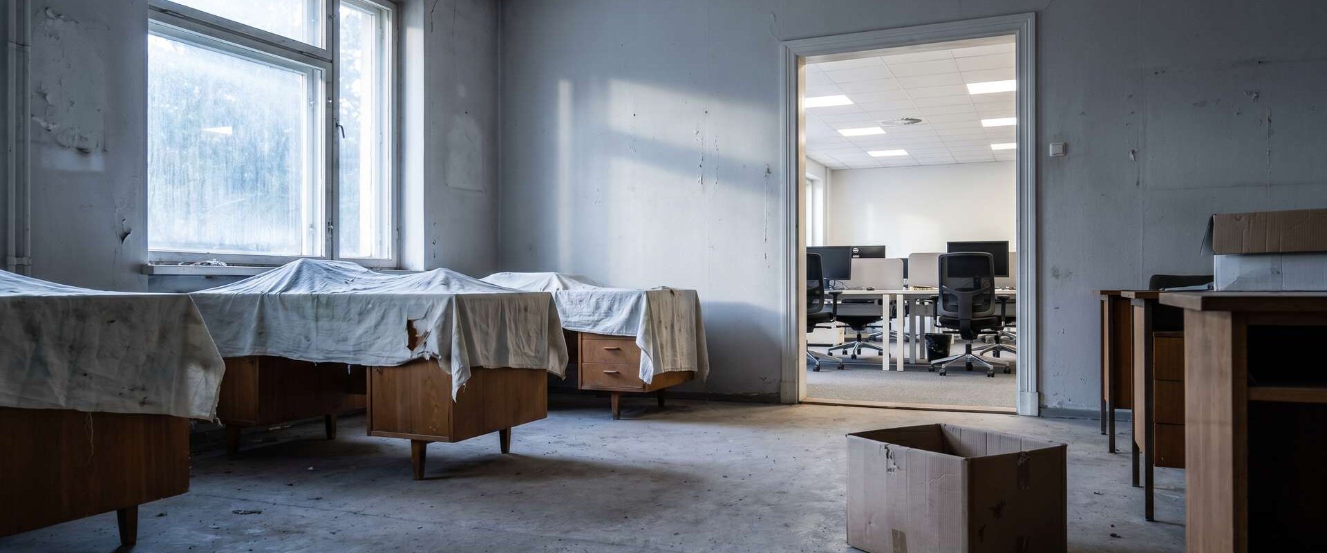 Leeres stillgelegtes Büro mit abgedeckten Schreibtischen, dahinter ein helles Büro